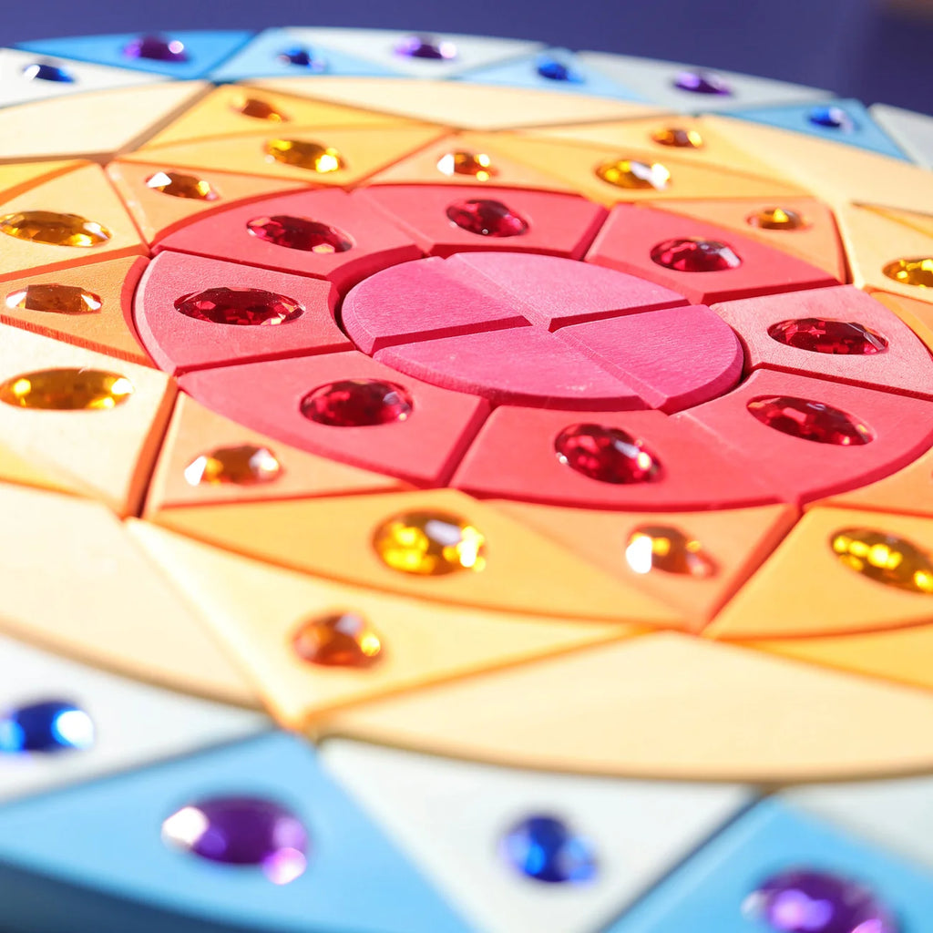 A Grimm’s Sparkling Mandala Sun Creative Puzzle featuring a circular wooden design in a mandala pattern with colorful geometric segments embedded with faceted jewels, perfect for developing fine motor skills.