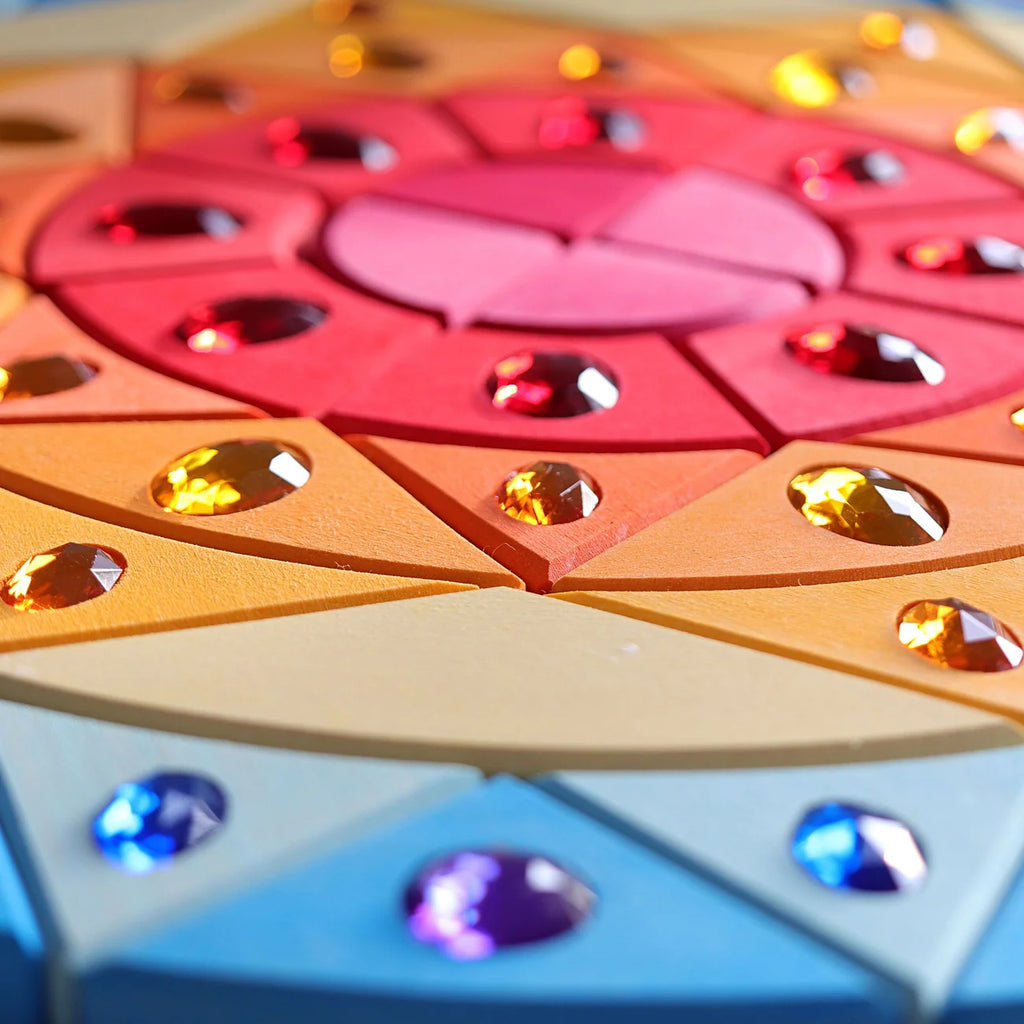 Grimm’s Sparkling Mandala Sun Creative Puzzle pieces are arranged in a circular mandala pattern, featuring inlaid colorful acrylic gemstones to support fine motor skills.