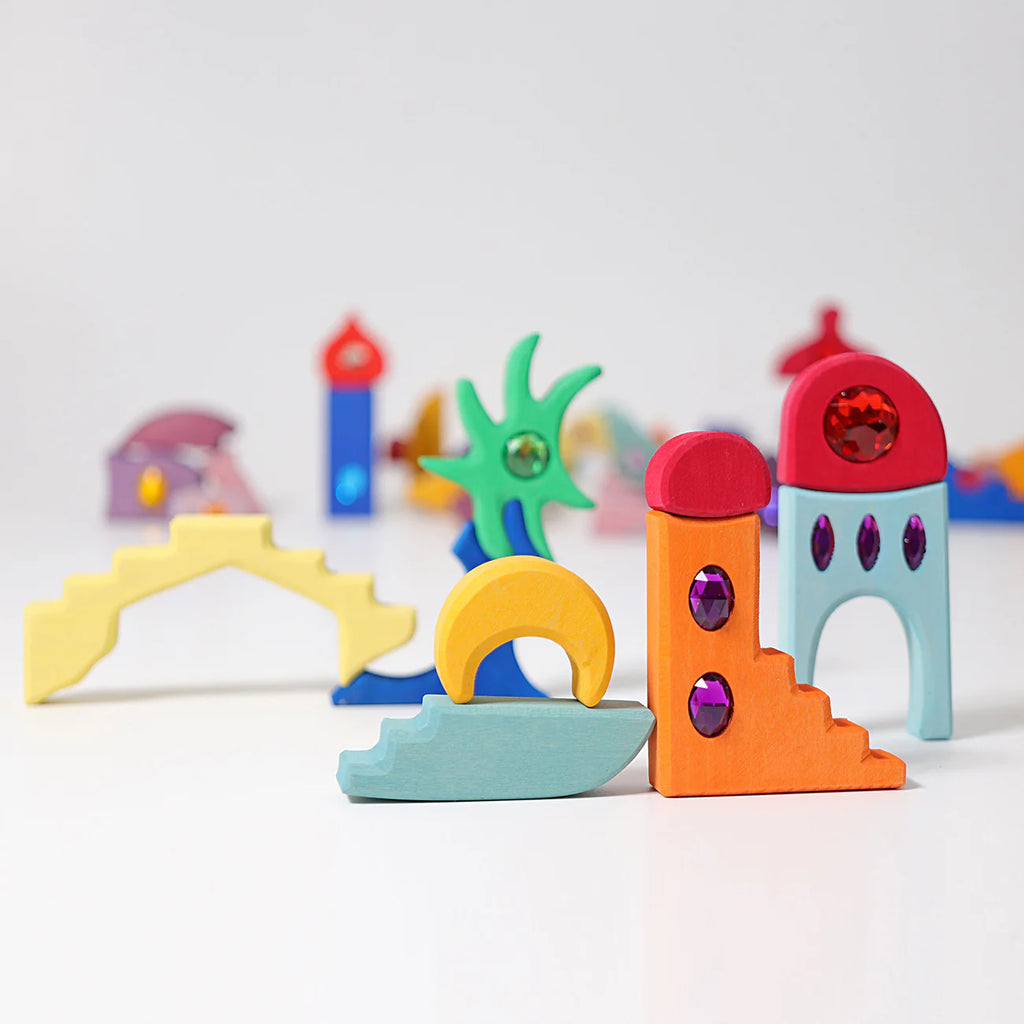 Grimm's Sparkling Mandala Orient features colorful glitter wooden blocks in shapes like arches, stairs, and abstract forms, some with sparkling mandala decorations. Creatively arranged on a white background. Ships in 1-2 weeks.