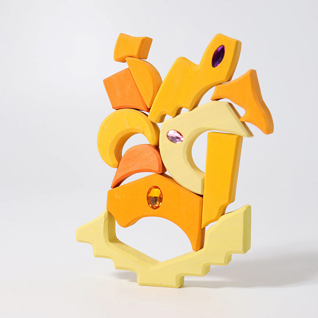 Grimm's Sparkling Mandala Orient, a set of colorful yellow and orange wooden blocks with glittering stones, is artistically stacked against a plain white background. Ships in 1-2 weeks.