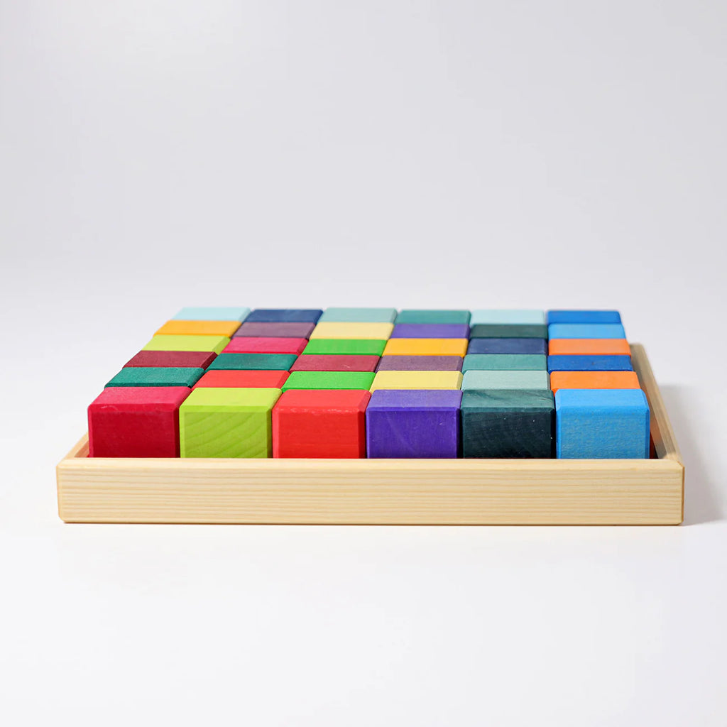 Grimm's Rainbow Mosaic Building Blocks are neatly arranged in rows within a wooden tray, displayed against a plain white background—ideal for encouraging spatial thinking and developing fine motor skills in young children.