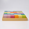 A wooden tray containing neatly arranged Grimm's Pastel Mosaic Building Blocks. The blocks are organized in a grid pattern, featuring colors such as pink, blue, orange, yellow, purple, and green. This delightful arrangement helps children develop fine motor skills against a plain white background.