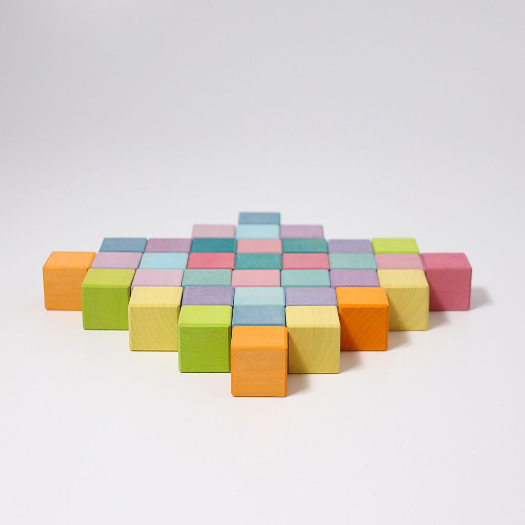 This image shows an arrangement of Grimm's Pastel Mosaic Building Blocks on a white surface. The blocks, perfect for developing children's fine motor skills, are in various pastel colors like green, orange, yellow, blue, purple, and pink. They are organized to form a stepped, diagonal pattern.