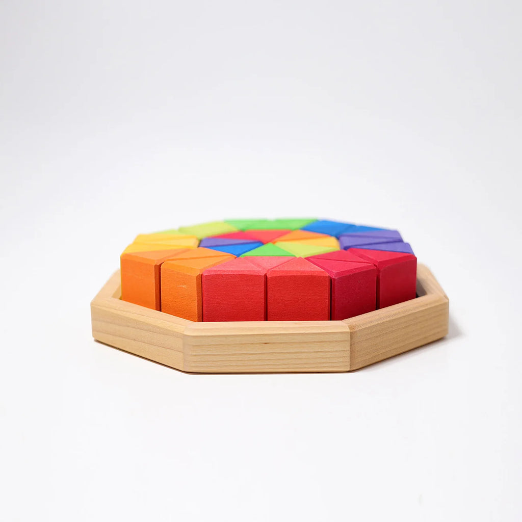 Grimm’s Medium Octagon (ships in 2-3 weeks) features a sturdy wooden octagonal tray that holds colorful geometric building blocks arranged in a circular pattern. The blocks display vibrant shades of red, orange, yellow, green, and blue against a plain white background.