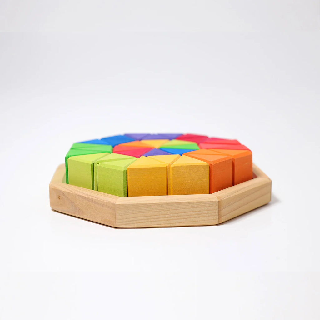 Grimm’s Medium Octagon (ships in 2-3 weeks) features a sturdy wooden octagonal tray filled with vibrant geometric building blocks arranged in a colorful rainbow pattern—including red, orange, yellow, green, blue, and purple sections. The set also includes triangle-shaped toy pieces, perfect for creative play and learning on a white background.