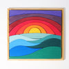 A Grimm's Creative Puzzle Landscape Block Set depicting a vibrant sunset over the ocean, with layered pieces creating the sky in shades of purple, red, and orange, and the ocean in shades of blue and green. This non-toxic puzzle is perfect for enhancing fine motor skills and is framed with a wooden border.