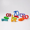 Grimm's Building Set - Numbers features colorful blue, green, yellow, orange, red, and purple digits scattered on a white surface. The upright number 4 is in the center—ideal for building and stacking to boost motor skills.