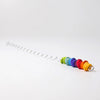 The Grimm's Spirelli Clatter Wand, a spiral metal rod adorned with vibrant wooden beads stacked in rainbow sequence at one end—evoking the look of cascading rings from a classic wooden spiral toy—rests against a plain white background.