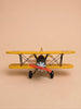 A front view of Little Forest Animals — The Aviator, a yellow handcrafted metal biplane featuring a red propeller, is set against a plain beige background, evoking the charm of a classic model airplane.