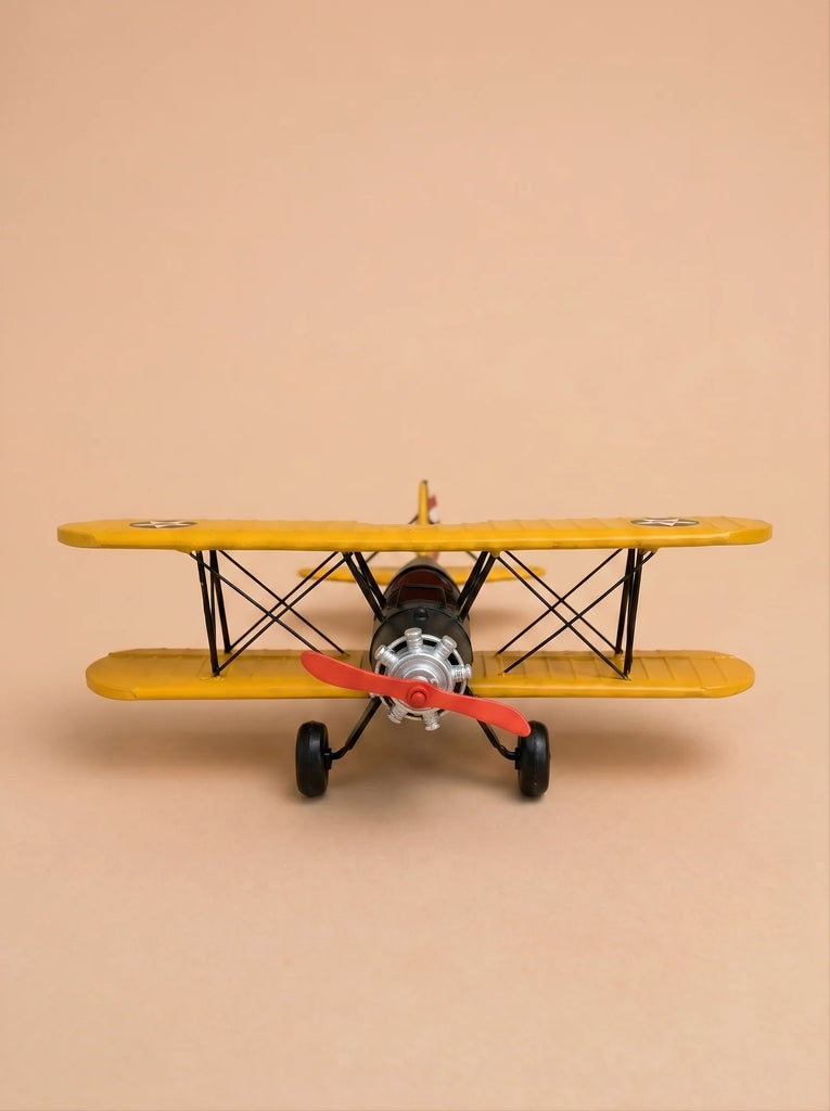 A front view of Little Forest Animals — The Aviator, a yellow handcrafted metal biplane featuring a red propeller, is set against a plain beige background, evoking the charm of a classic model airplane.