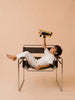 A young boy in white clothes reclines on a modern chair, holding Little Forest Animals — The Aviator handcrafted metal biplane above him against a beige background.