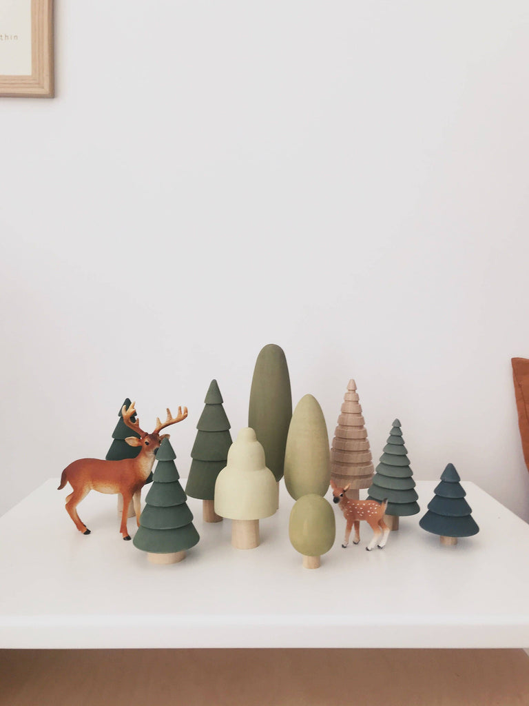 The Wooden Forest Set includes a variety of SABO concept toys, such as wooden toy trees in different shapes and shades of green, along with two small deer figures. Ideal for imaginative play, these pieces are arranged on a white surface with a plain white background.