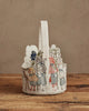 The Coral & Tusk Easter Parade Basket, a felt basket with a handle and detailed embroidered deer, cat, fox, and rabbit in clothes, stands upright on a rustic wooden surface against a neutral background.