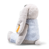 The Steiff Hoppie Rabbit in Ski Outfit, 12 inches, features light gray fur, long floppy ears, and a soft blue patch on its back. It sits upright facing away with a yellow tag hanging from its left ear.
