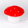 The Red Mushroom Lamp is a whimsical night light with a white stem and red cap topped with white spots, ideal for adding charm to any child's room or nursery. Displayed on a plain white background.