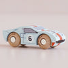 A No. 26 GT145 Fred wooden racing car, crafted in England, featuring a light blue body with the number 6 on the door and hood, black windows, and natural wood wheels, displayed on a light surface.