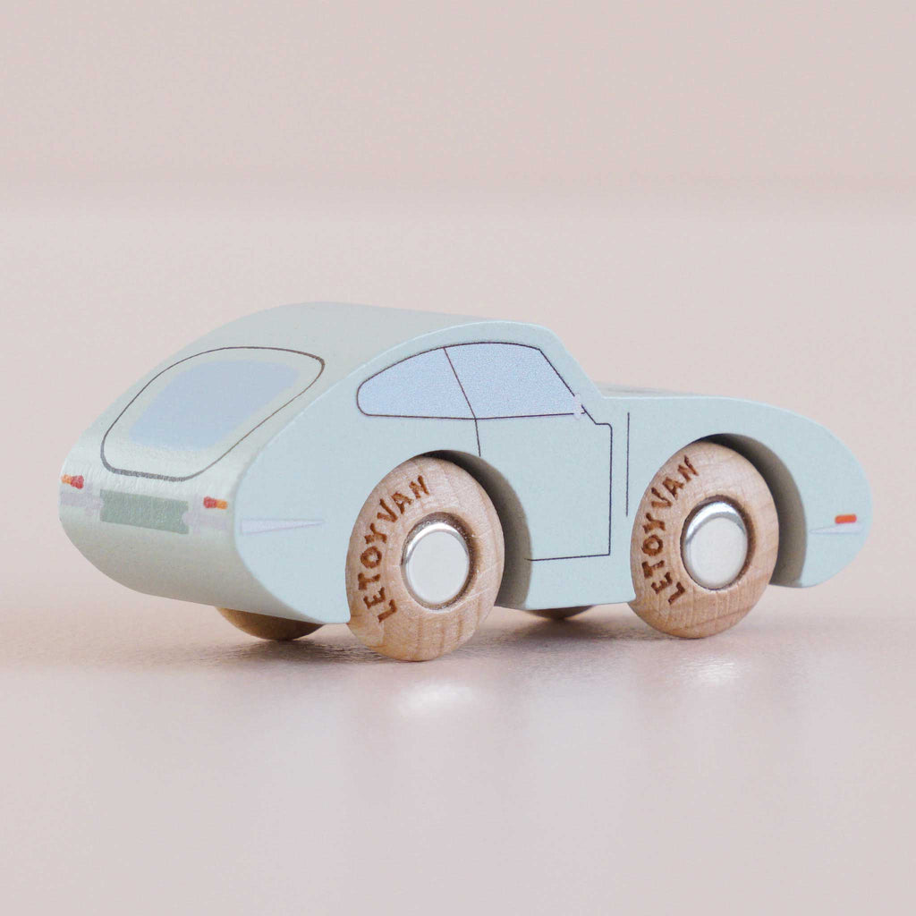 The No. 2 GT15 Jude, made in England, is a small, light blue vintage wooden car featuring simple painted details and wooden wheels, displayed on a smooth, light-colored surface—an ideal gift for kids who appreciate classic playthings.