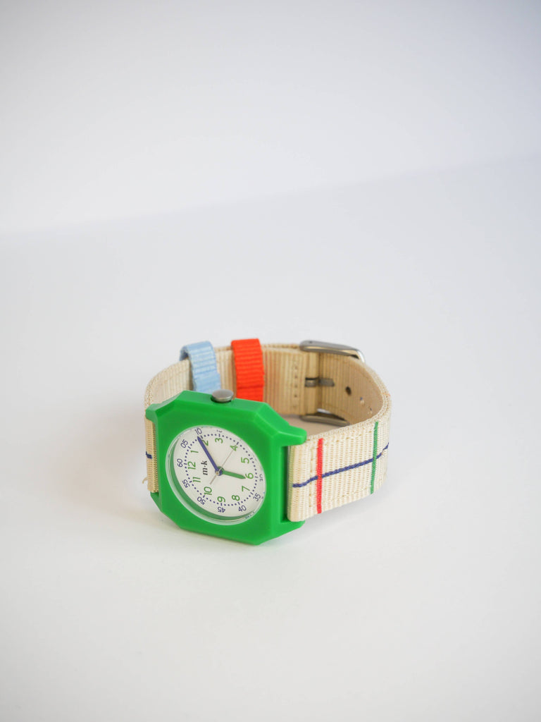 The Mini Kyomo Watch x Taxi Brousse - Color Notebook is a vintage style kids watch with a green plastic case and a cream fabric strap featuring red, blue, and green stripes, shown on a white background.