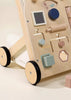 The Wooden Activity Walker features black wheels and a variety of interactive shapes, buttons, and mirrors in pastel colors, offering an engaging activity walker filled with sensory toys for play and development.