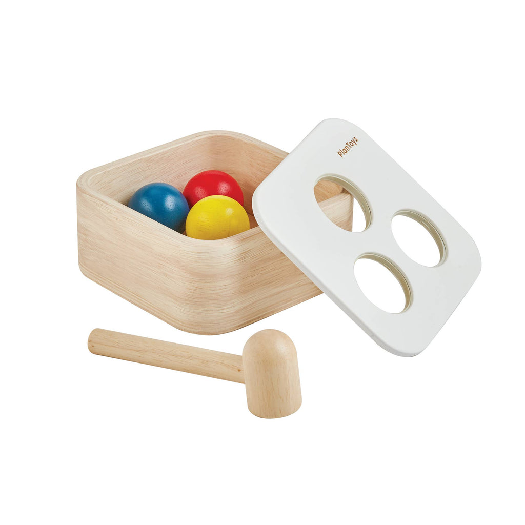 The Punch & Drop Bin is a classic cause and effect toy that includes a wooden set with three colored balls, a rectangular box, a white lid with three holes, and a sturdy wooden mallet.