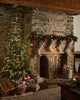 A cozy stone fireplace with stockings and garland sits beside a lit Christmas tree decorated with ornaments, including the Coral & Tusk Togetherness Deer Ornament. Wrapped gifts beneath the tree complete this festive holiday scene.