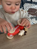 A young child in a beige sweater plays with a Wooden Race Car Toy with Dog Driver from Egmont Toys on a light wooden table.