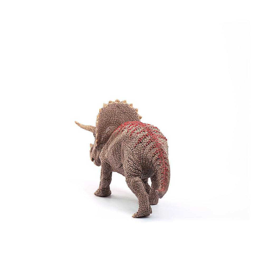 The Schleich Triceratops Dinosaur Toy features textured brown skin with red markings and is shown standing on a white background, facing away from the camera. This educational figurine provides realistic details for imaginative play or display.