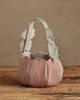 The Coral & Tusk Jack-o'-Lantern Basket features a soft, pleated fabric body in muted pink tones with a handle detailed in white leaves, blending style and Halloween charm. Ships in one week. Displayed on wood against a beige background.