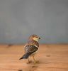 The Hand Carved Ornament - Sparrow Bird - 3.5"H features brown, black, and white feathers and stands on a wooden surface with its back to the camera against a gray background.