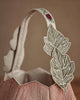 A close-up of the Coral & Tusk Jack-o'-Lantern Basket, showing a cream handle with embroidered green leaves and a red flower, and a textured reddish-brown body with vertical lines. Ships in one week.
