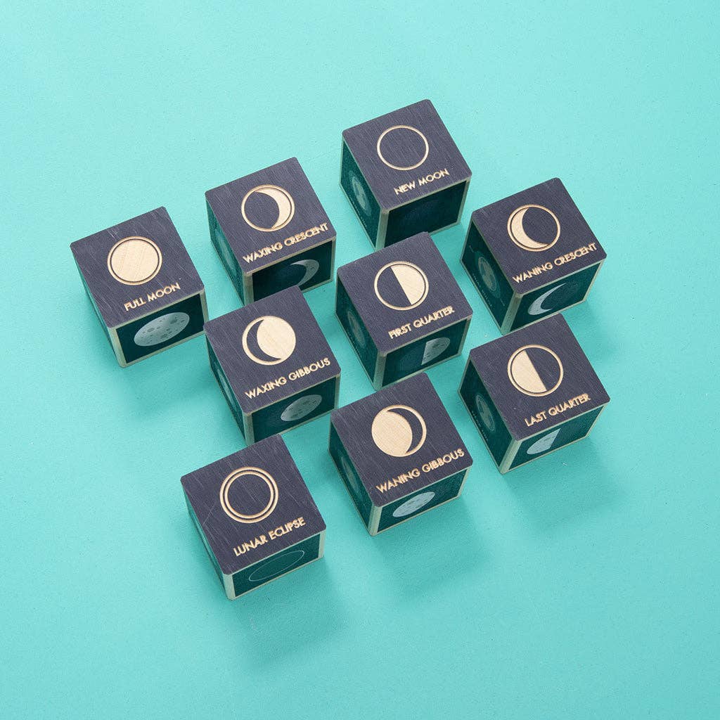 The Uncle Goose Moon Phase Blocks set features nine wooden blocks, each labeled with a different lunar phase—including New Moon, Full Moon, Lunar Eclipse, Waxing Crescent, First Quarter, Waxing Gibbous, Waning Gibbous, Last Quarter, and Waning Crescent—beautifully arranged on a teal background.