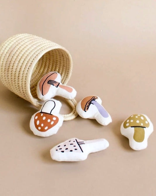 A collection of cute plush vegetables and the Mini Mushroom Basket spilling out from a small hand-woven basket, set against a plain beige background.