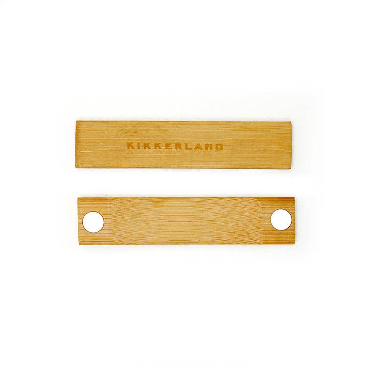 The Huckleberry Grass Whistle set features two rectangular bamboo sticks on a white background—one engraved with "KIKKERLAND," the other designed for whistle sounds with two round holes. Ideal for outdoor hiking adventures.