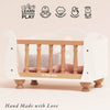 A Wooden Dolls Cot made of white wood with natural spindles, featuring a soft pink bedding set, displayed with five developmental skill icons above and the text “Hand Made with Love” below.