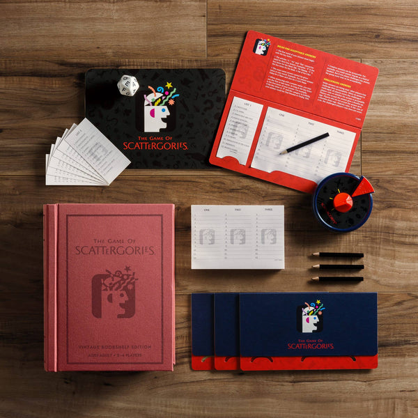 The Board Game: Scattergories Vintage Bookshelf Edition comes with a red box, player pads, answer sheets, black pencils, a timer, 20-sided die, and instructions—neatly displayed on a wooden surface.