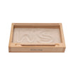 The Sand Tray with Flash-Card Holder is a rectangular wooden Montessori tray filled with fine sand, perfect for developing writing skills. The letters "WS" are drawn in the sand. A wooden stick rests on the front edge of the tray, which is labeled "Wooden Story." This educational toy combines learning and play beautifully.