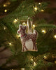 The Coral & Tusk Rudolph Ornament, featuring white spots and a red collar, hangs from a lit Christmas tree branch, adding festive flair to your holiday décor.