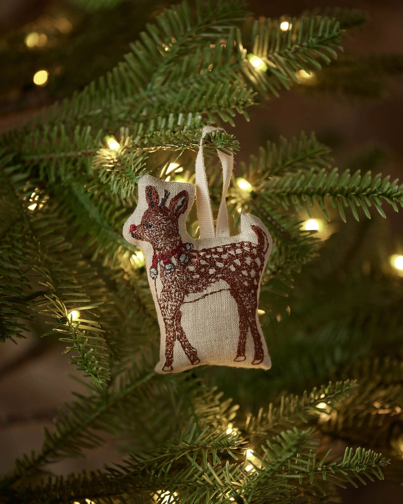 The Coral & Tusk Rudolph Ornament, featuring white spots and a red collar, hangs from a lit Christmas tree branch, adding festive flair to your holiday décor.