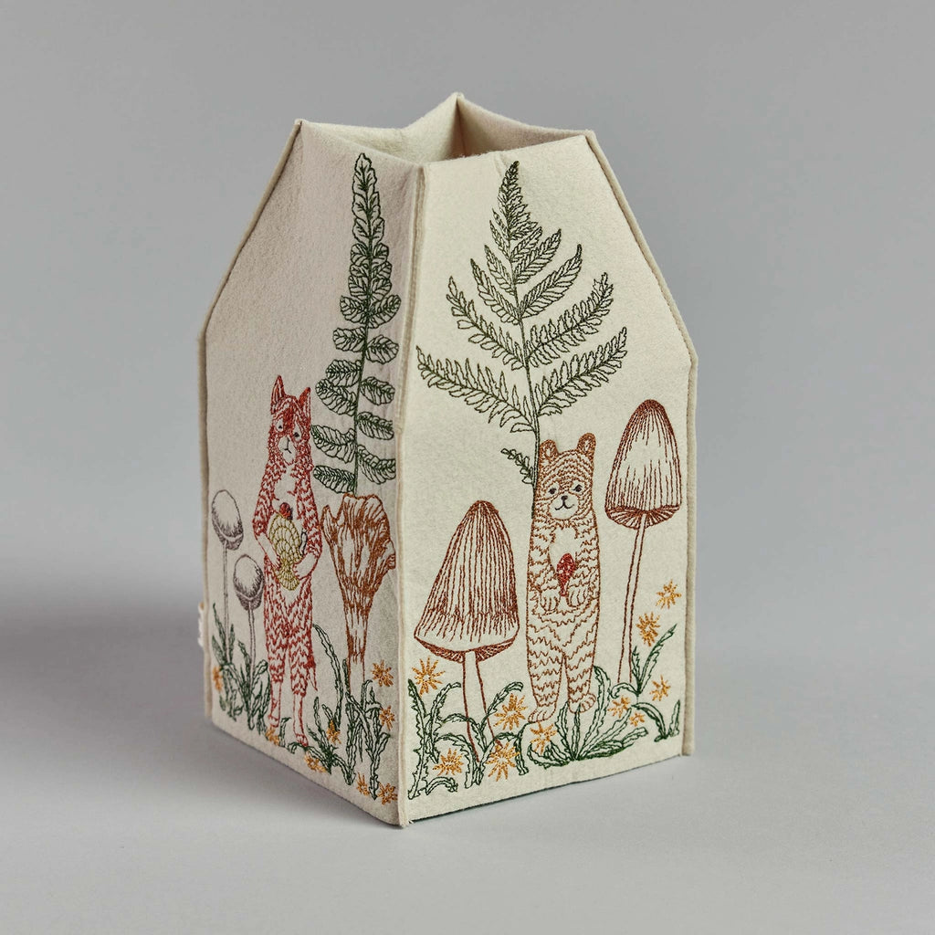 An embroidered Coral & Tusk Mushrooms and Ferns tissue box cover shaped like a house, featuring detailed woodland scenes including a fox, a rabbit, ferns, and mushrooms on a neutral background.