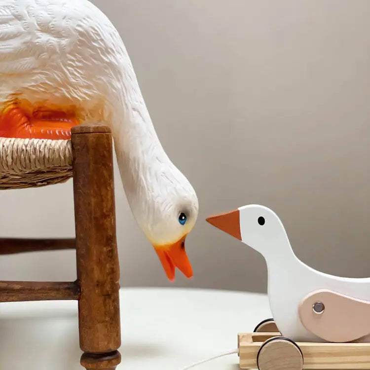 The Duck Looking Down Lamp features a charming duck figure leaning down as if to touch beaks with a smaller pull-toy duck, making it an adorable accent for children's room decor against a plain light background.