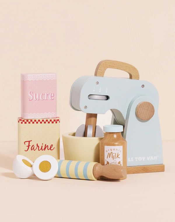 The Bakers Mixer Set & Accessories is a pastel wooden toy mixer set with a mixing bowl, eggs, rolling pin, milk carton, and "Sucre" and "Farine" containers—ideal for imaginative kitchen play against a light beige background.