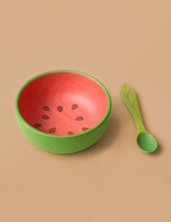 Wally the Watermelon Bowl & Spoon Set features a round wooden baby bowl with a green exterior and red, seed-patterned interior, paired with a leaf-patterned green spoon—a charming, non-toxic addition to your baby's tableware.
