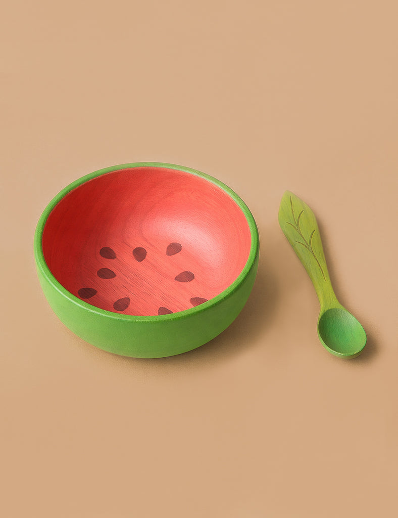 Wally the Watermelon Bowl & Spoon Set features a round wooden baby bowl with a green exterior and red, seed-patterned interior, paired with a leaf-patterned green spoon—a charming, non-toxic addition to your baby's tableware.