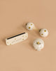 The Konges Sloejd Petit Music Set - Glossy Lemon, featuring three small cream-colored wooden instruments with yellow lemon patterns—a harmonica, kids’ maracas, and a jingle bell—rests on a light beige background.