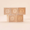 Five Uncle Goose Number Alphablank Blocks, each with a carved design, display the equation 6 ÷ 2 = 3. The educational toys are stacked in two rows against a neutral background.