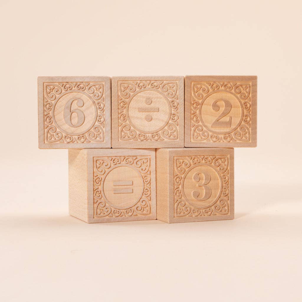 Five Uncle Goose Number Alphablank Blocks, each with a carved design, display the equation 6 ÷ 2 = 3. The educational toys are stacked in two rows against a neutral background.