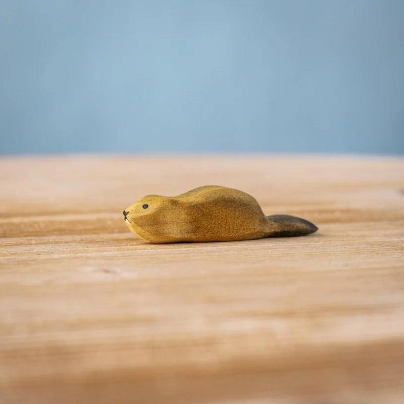 The Bumbu Handmade Wooden Baby Beaver, an eco-friendly Montessori toy, is displayed on a light wooden surface against a blurred blue background.