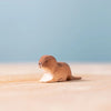 The Bumbu Handmade Wooden Baby Otter, an eco-friendly toy, sits charmingly on a light wooden surface against a soft blue background.