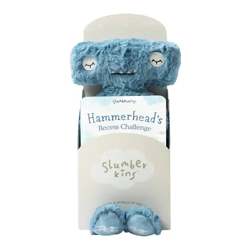 An image of a plush toy named Slumberkins Hammerhead Kin + Lesson Book - Conflict Resolution. The toy is blue with a soft texture, sleepy eyes, and subtly patterned feet. It is packaged with a book titled "Hammerhead's Recess Challenge," providing a bedtime story that encourages emotional regulation and social skills development.