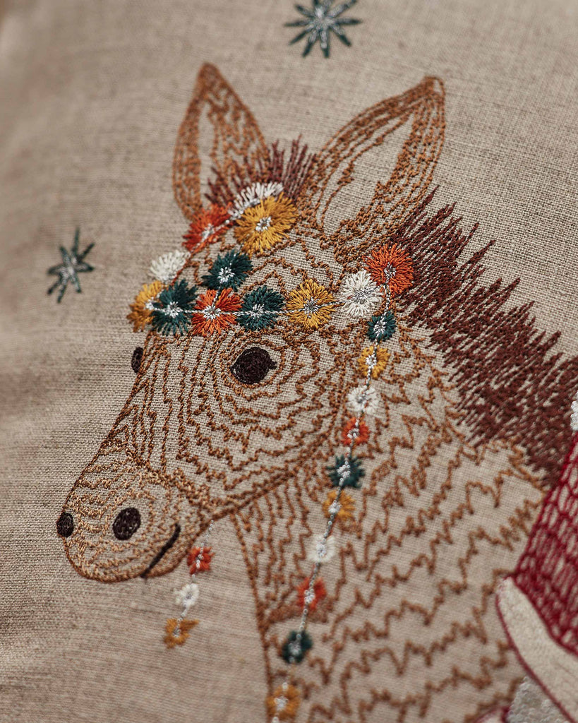 Intricate embroidery of a donkey's head on beige fabric with colorful flowers and star-like accents—perfect as festive holiday decor or a charming touch to a Christmas toy basket. Introducing the Christmas Donkey Pillow!.